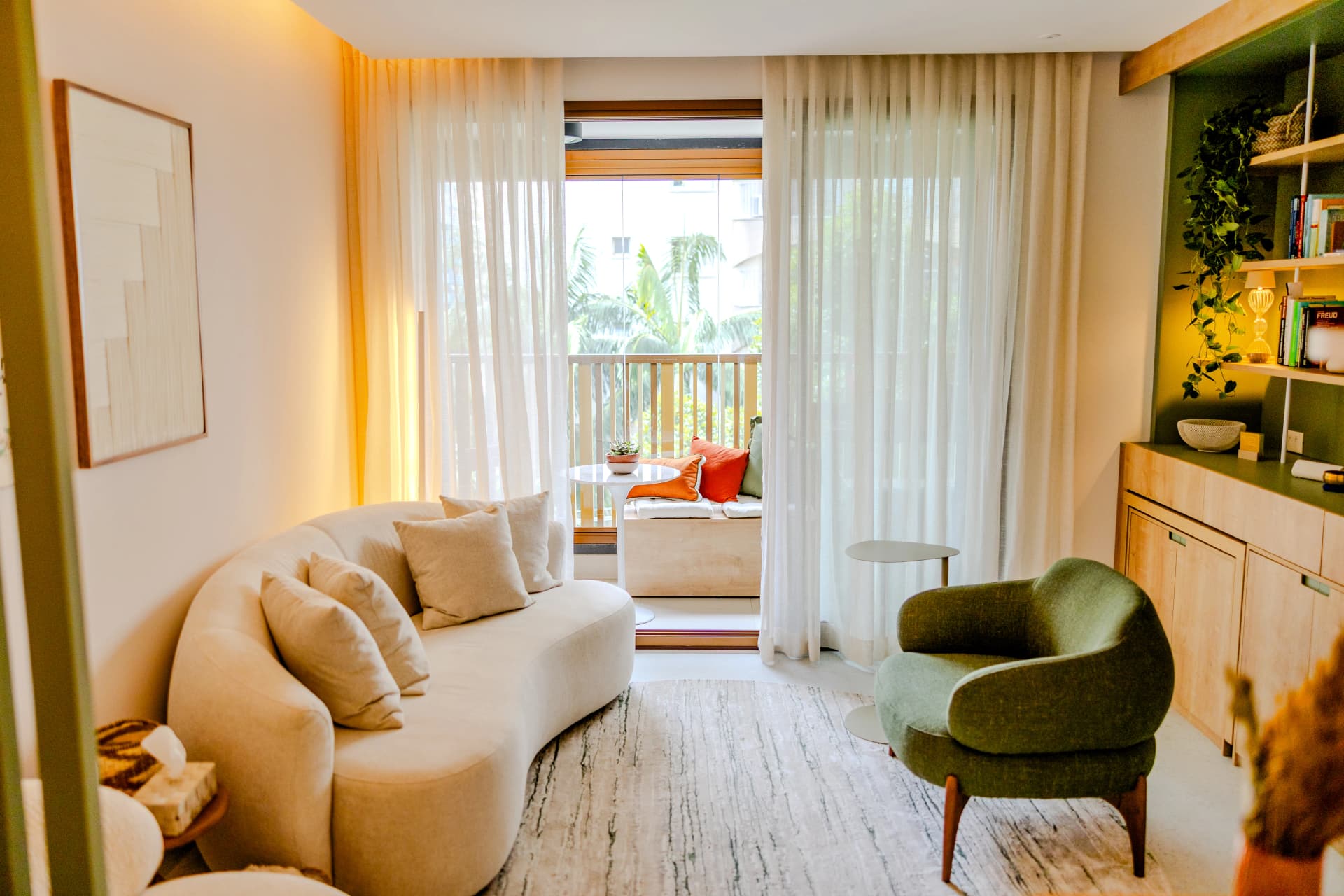 Sala ampla com sofá creme, poltrona verde e porta de vidro com vista para varanda