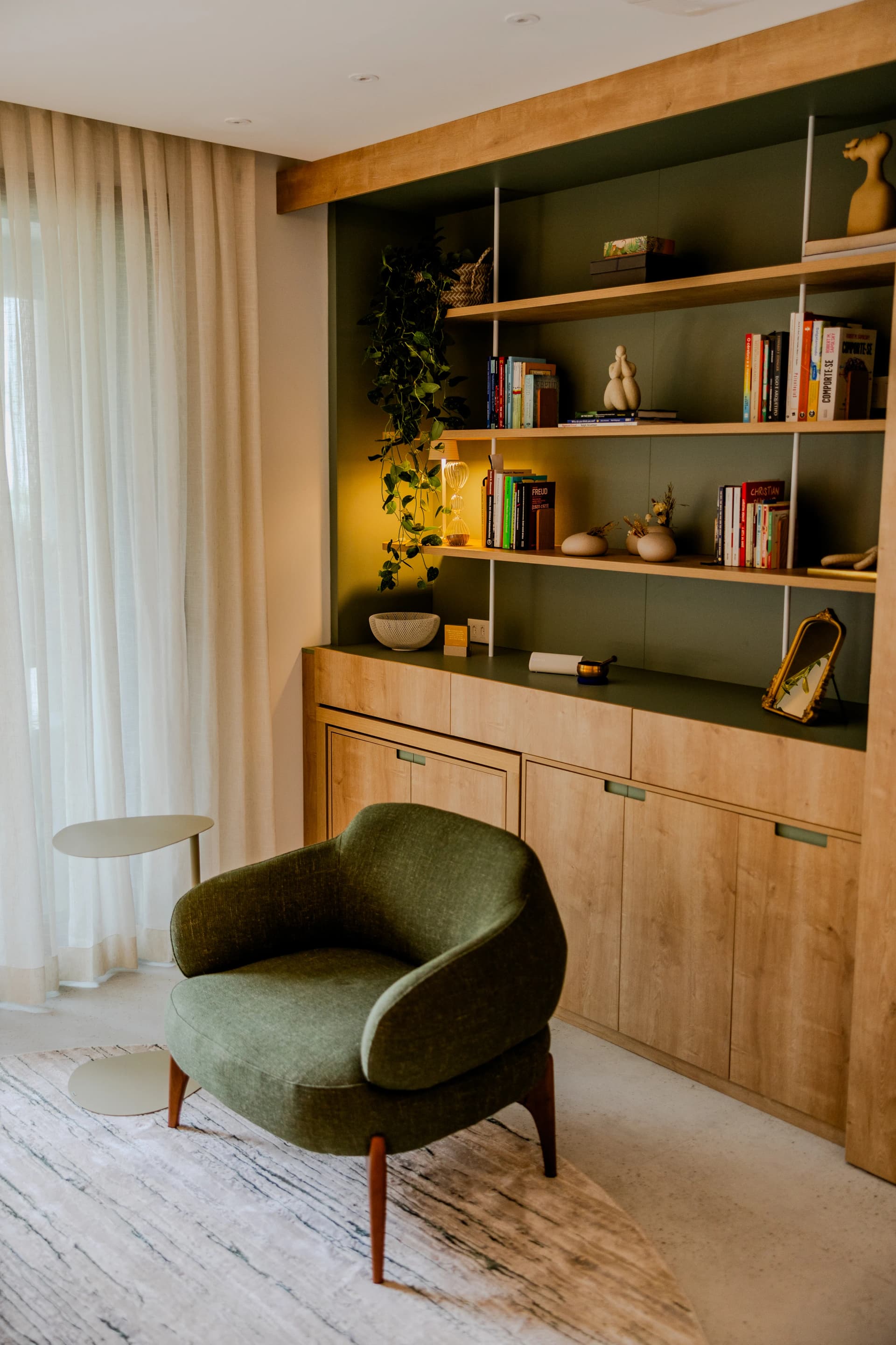 Mesa lateral minimalista e poltrona verde no consultório de psicologia acolhedor